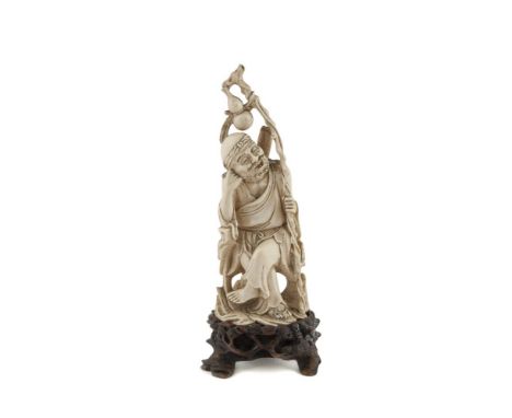 A 19TH CENTURY JAPANESE CARVED IVORY OKIMONO, modelled as an elderly man, seated and holding a gnarled staff from which hangs