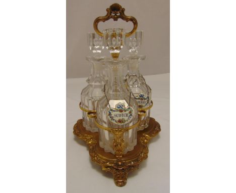 A gilt metal three bottle decanter stand, trefoil on three shell feet, the cut glass decanters with drop stoppers and two ena