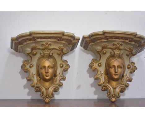A pair of parcel-gilt plaster wall brackets, c. 1900, each with shaped shelf above a female mask within c-scrolls. 27cm by 30