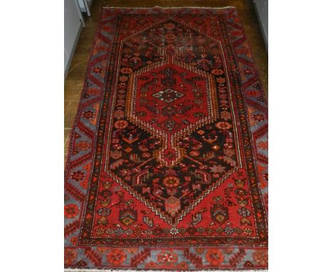 A red ground Caucasian carpet, decorated with stepped tear drop medallion to centre, on a stylised floral ground, within pale