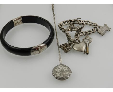 A silver charm bracelet, hallmarked London and A.G.C, together with a white metal and black bangle and a silver guilt locket 