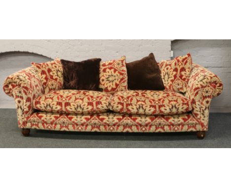 A good quality four seat sofa upholstered in red and gold velvet moquette upholstery raised on carved bun feet.