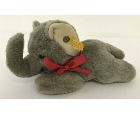 A Steiff laying down baby grey elephant. Red ribbon to neck and button to left ear.  Approx. 20 cm long.