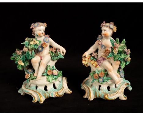 A pair of Bow porcelain seated cherub candlestick bases, circa 1765, applied garlands and bocage on pierced scroll bases, red