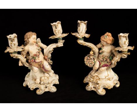 A pair of Chelsea gold anchor figural candlestick figures, Cupid and girl swathed in flowers on rococo scroll bases, circa 17