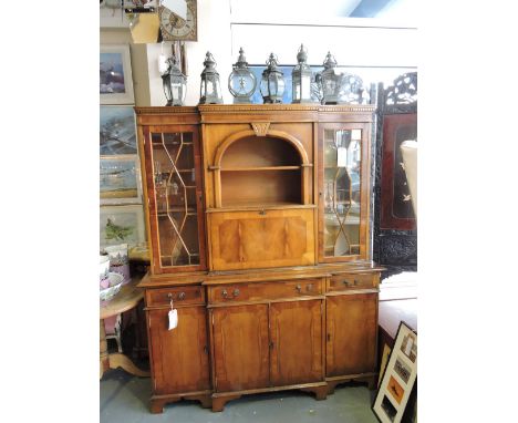 A George III style yew breakfront cabinet, the upper section with a central arched recess flanked by astragal doors, the base