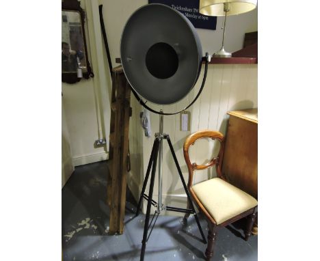 An industrial style black and chrome standard lamp with circular shade on adjustable tripod.