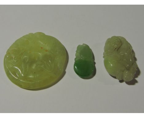 A Chinese carved jade pendant together with a similar larger green stone pendant and a circular green hardstone disc.