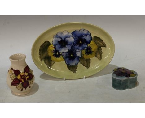 A Moorcroft Pansy pattern oval tray, 23cm wide; an Anemone pattern trinket pot and cover; a small baluster vase (3) 