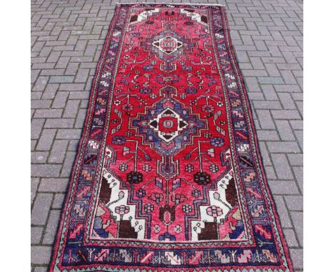 A hand woven Hamadan carpet, geometric and floral designs in tones of steel blue, cocoa brown and green on a muted pink groun