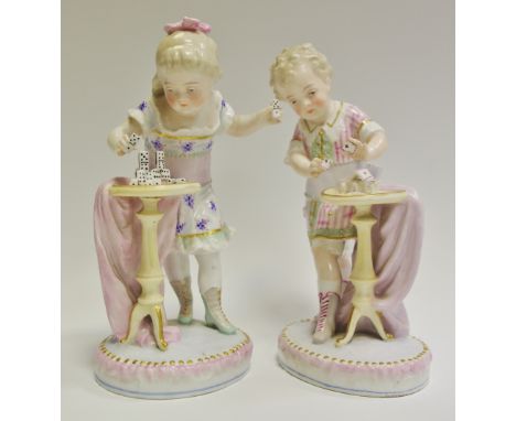 A pair of German figures, of a girl playing with dominoes and boy playing with playing cards, in pastel tones, 21cm high, mar