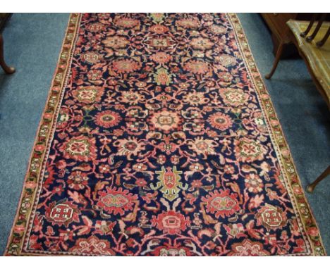 A hand woven Hamadan carpet, floral designs in tones of pink, brown and brick on a dark cobalt ground. 256cm x 150cm.