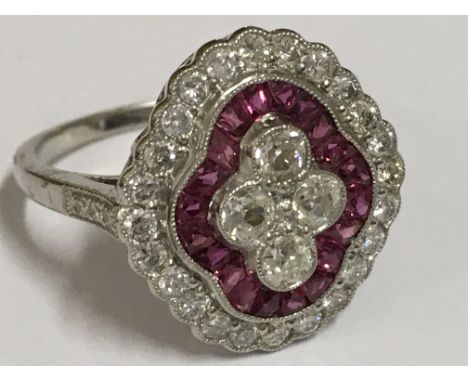 A Victorian-style platinum ruby and diamond ring. Set with four diamonds, centrally surround by calibre-cut rubies. The ring 