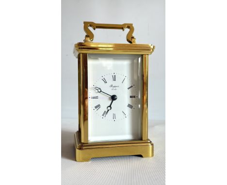 Brass carriage clock by Rapport London features a visible mechanism and Roman numeral dial, encased in glass with an ornate h