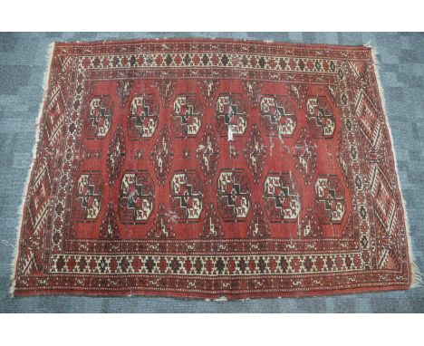 An antique red ground Bokhara wool rug, two rows of typical woven 'tiles', abstract floral pattern border, 153 cm by 115 cm. 