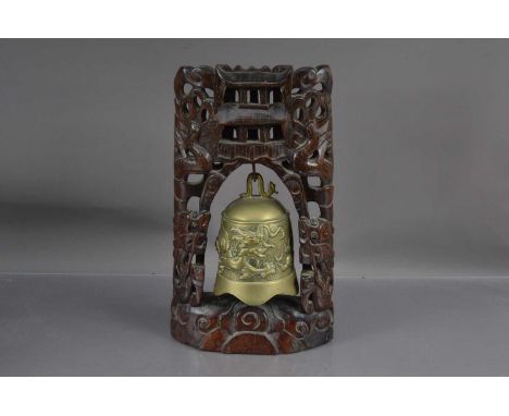 A Chinese brass bell or gong with a dragon chasing a flaming pearl, suspended within an associated hardwood stand carved with
