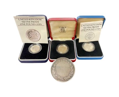 A mixed lot comprising three silver £1 proof coins and a Cambridge University medal.