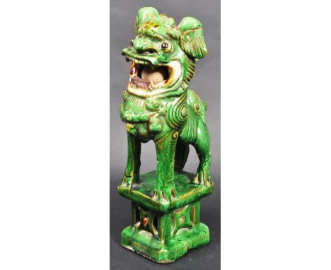A 19th Century Chinese ceramic figure of a temple Foo Dog / Dog of Fu moulded in a standing position holding the orb in his m