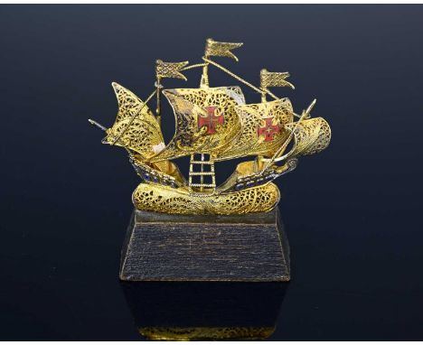 A twentieth-century gilt metal filigree miniature model of a sailing ship, with three masts and rigging, adorned with red ena