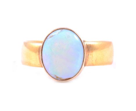 A 22 carat yellow gold 5.5mm wide band set with an oval cabochon cut opal 11.5x10mm, in a closed back setting, ring size U/V,