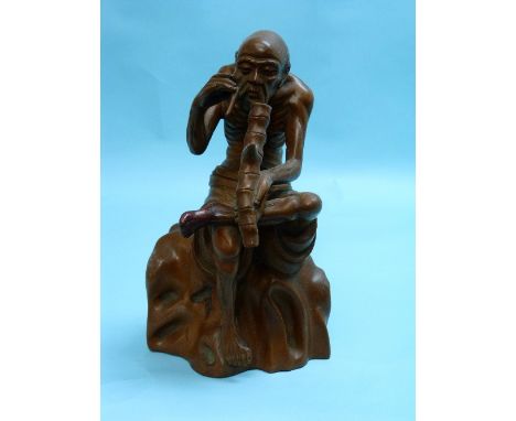 An Oriental Huangyang wood figure, depicting a man seated on rock with pipe, foot restored, 9in (23cm) high.