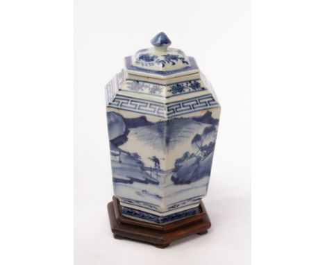 A Chinese hexagonal blue and white porcelain vase and lid on a wooden stand, Qing Dynasty, decorated floral, fruits and Huiwe