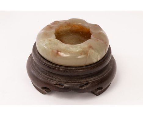 A Chinese celadon jade water vessel carved in the form of a lily pad, Ming dynasty, on a wooden stand, 6cm diameter CONDITION