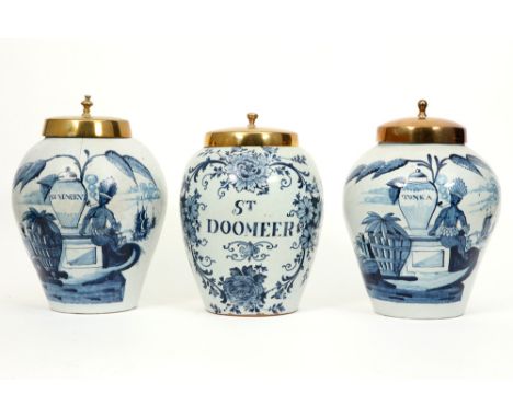 three 18th Cent. ceramic tobacco jars (two are marked) from Delft with a blue-white decor and brass lid || Lot van drie achtt