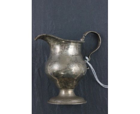 A Georgian hallmarked silver cream jug; of helmet form; with beadwork decoration and 'S' scroll handle; hallmarks rubbed