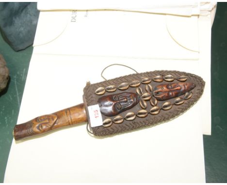 A tribal dagger, the wooden hilt carved with a mask in a sheath, applied with cowrie shells and carved wooden masks