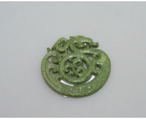 A circular pierced Spinach jade pendant carved with a dragon, 7cm diameter