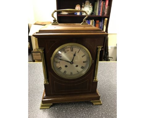 An Edwardian inlaid mantel clock with brass column pilasters and feet, the silvered dial to the eight-day movement striking o
