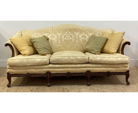 An early 20th century camel back sofa of Georgian design, upholstered in gilt floral damask fabric, enclosing a floral carved