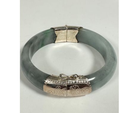 A Chinese white metal mounted circular grey/ celedon coloured Jadite bangle with engraved water lily and leaf design to mount