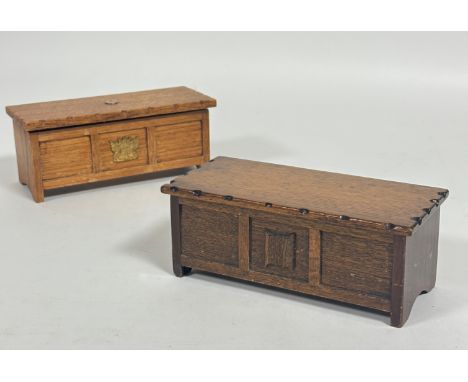 An oak miniature coffer style kist cigarette box, the hinged top enclosing a twin section with brass plaque to front and enam