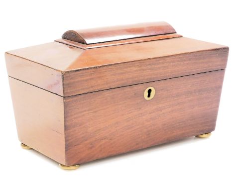 A Regency mahogany sarcophagus form tea caddy, the hinged lid opening to reveal twin lidded compartments, raised on brass bun