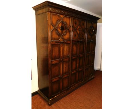 A late Victorian oak compactum wardrobe, by James Shoolbred of London, the outswept pediment with dentil moulding, above a fl