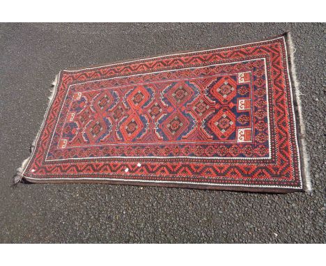 A vintage Afghan handmade wool rug with repeat gul motifs within a double border on red ground - 1.84m X 1.01m