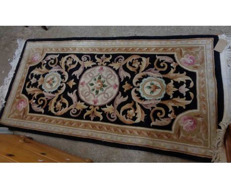 A modern Chinese handmade washed wool rug with roundel and scroll decoration within a shaped border on black ground - 1.9m X 