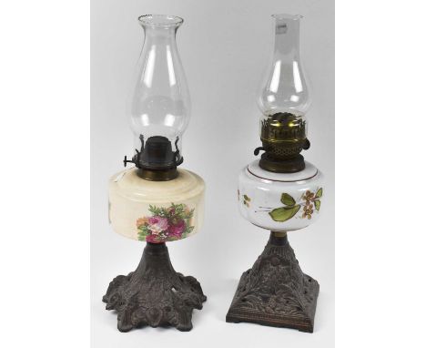 Two Victorian oil lamps with decorative cast iron bases, one with floral decorated ceramic bowl the other painted glass, with