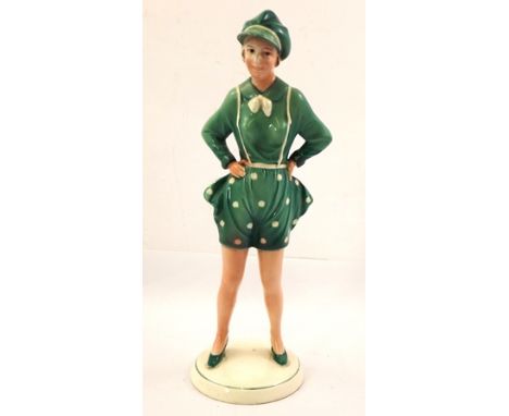 A "KATSHUTE" ART DECO CERAMIC FIGURINE of a young woman modelled with her hands upon her hips, wearing a green costume with p