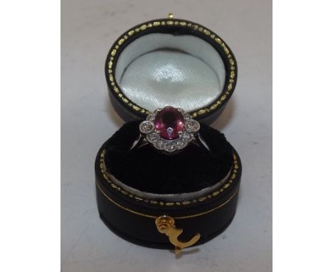 A RUBY AND DIAMOND CLUSTER RING, having oval central stone bordered by twelve brilliants, on plain polished shank, size M 1/2