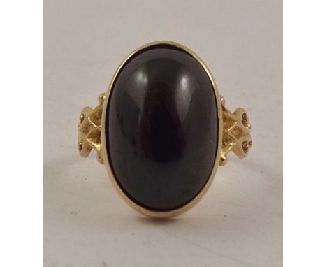 AN ART NOUVEAU STYLE DRESS RING, having oval cabochon garnet in rub-over surround with stylized shoulders, stamped 9ct, ring 