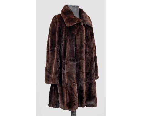 Knielanger, gerade geschnittener Mantel aus dunkelbraunem, geschorenem Nerz mit Rundkragen und seitlichen Taschen. Violettes 