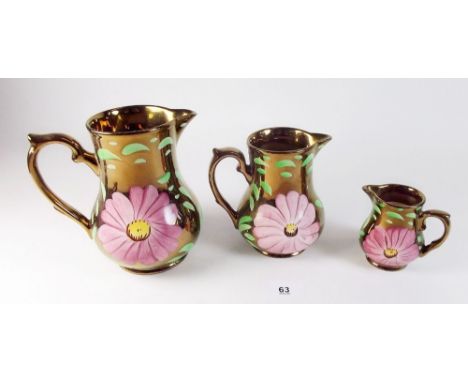 A Wade set of three graduated copper lustre jugs with painted floral decoration