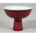 A SMALL CHINESE RED GLAZE PORCELAIN STEM CUP, the interior with blue and white floral motif, the