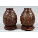 A PAIR OF JAPANESE HEAVY BRONZE VASES with hardwood stands, with relief floral decoration, the bases