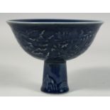 A CHINESE SACRIFICIAL BLUE GLAZE PORCELAIN STEM CUP, the exterior with raised decoration depicting