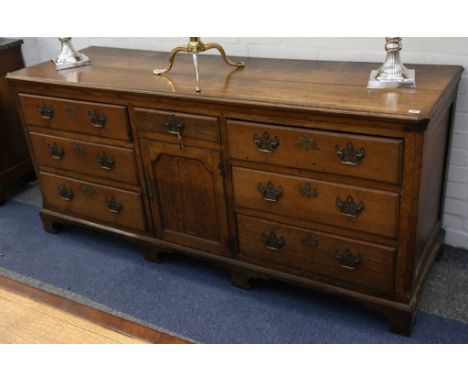 An antique oak dresser base, with an arrangement of various sized drawers around a central cupboard on bracket feet, 190cm wi