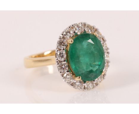 An emerald and diamond cluster ring, the oval shaped mixed cut emerald weighing 3.58cts, claw set within a brilliant cut diam